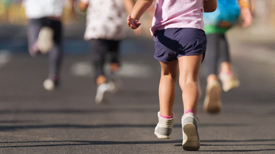 Crianças simulam uma corrida. Uma menina, vestida de blusa rosa e bermuda azul, aparece na imagem destacada, enquanto os outros desfocados na imagem. A imagem ilustra o evento promovido por uma Associação, que pretende conscientizar sobre o tratamento adequado de Pé Torto Congênito. 